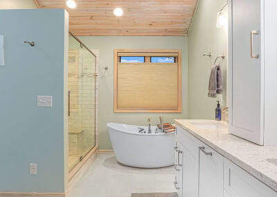 Wide view of New Bathroom Layout with vanities in foreground and tub and glass shower in distance